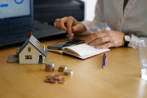 Pessoa fazendo contas ao lado de uma miniatura de casa